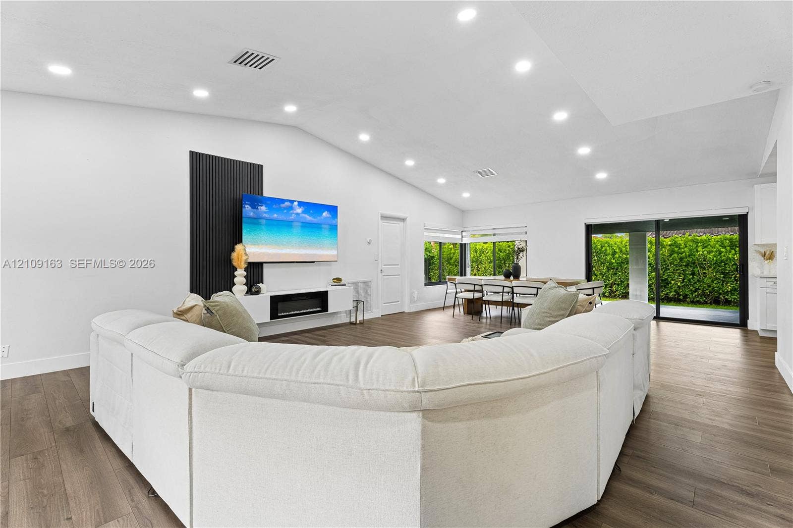 9122 SW 127th Avenue, Miami, FL 33186 Open-concept interior featuring vaulted ceilings, wood-finish flooring, recessed lighting, a built-in electric fireplace with vertical slat wall detailing, and sliding glass doors