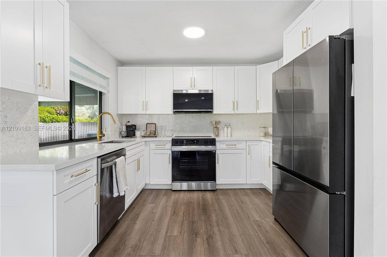 9122 SW 127th Avenue, Miami, FL 33186 Kitchen featuring shaker-style white cabinetry, quartz countertops, stainless steel appliances, brass-finish hardware, and wood-finish flooring