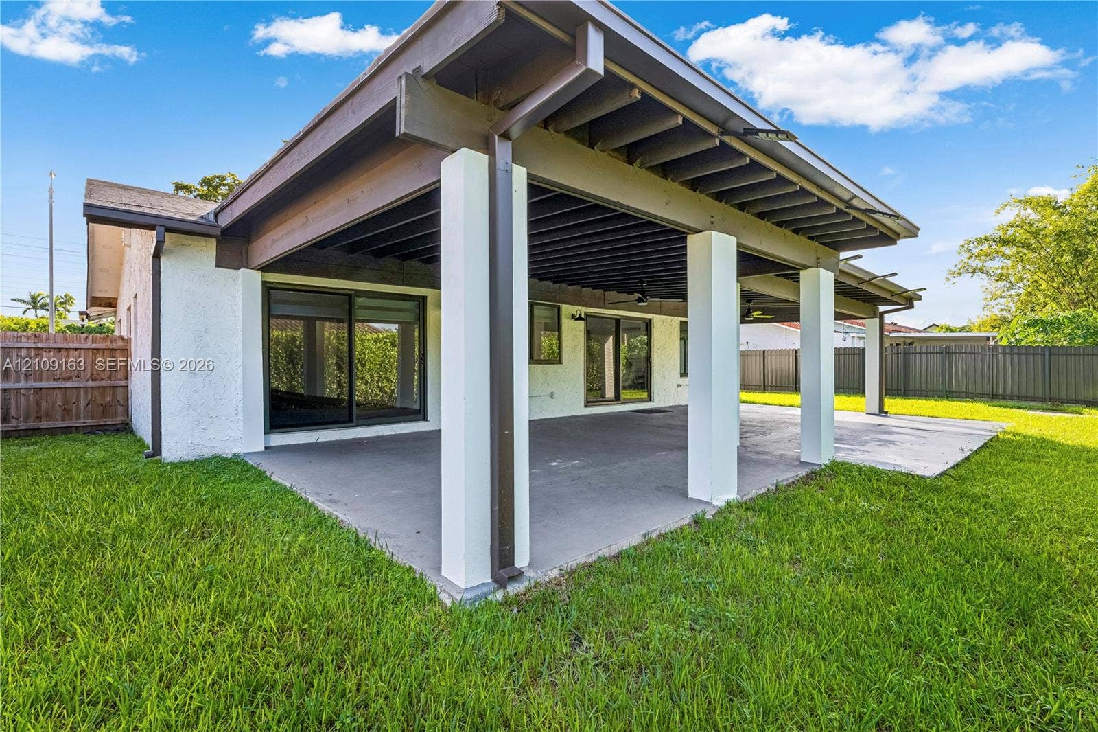 9122 SW 127th Avenue, Miami, FL 33186 Covered outdoor patio featuring exposed wood-beam ceiling, concrete flooring, square structural support columns, and sliding glass door access
