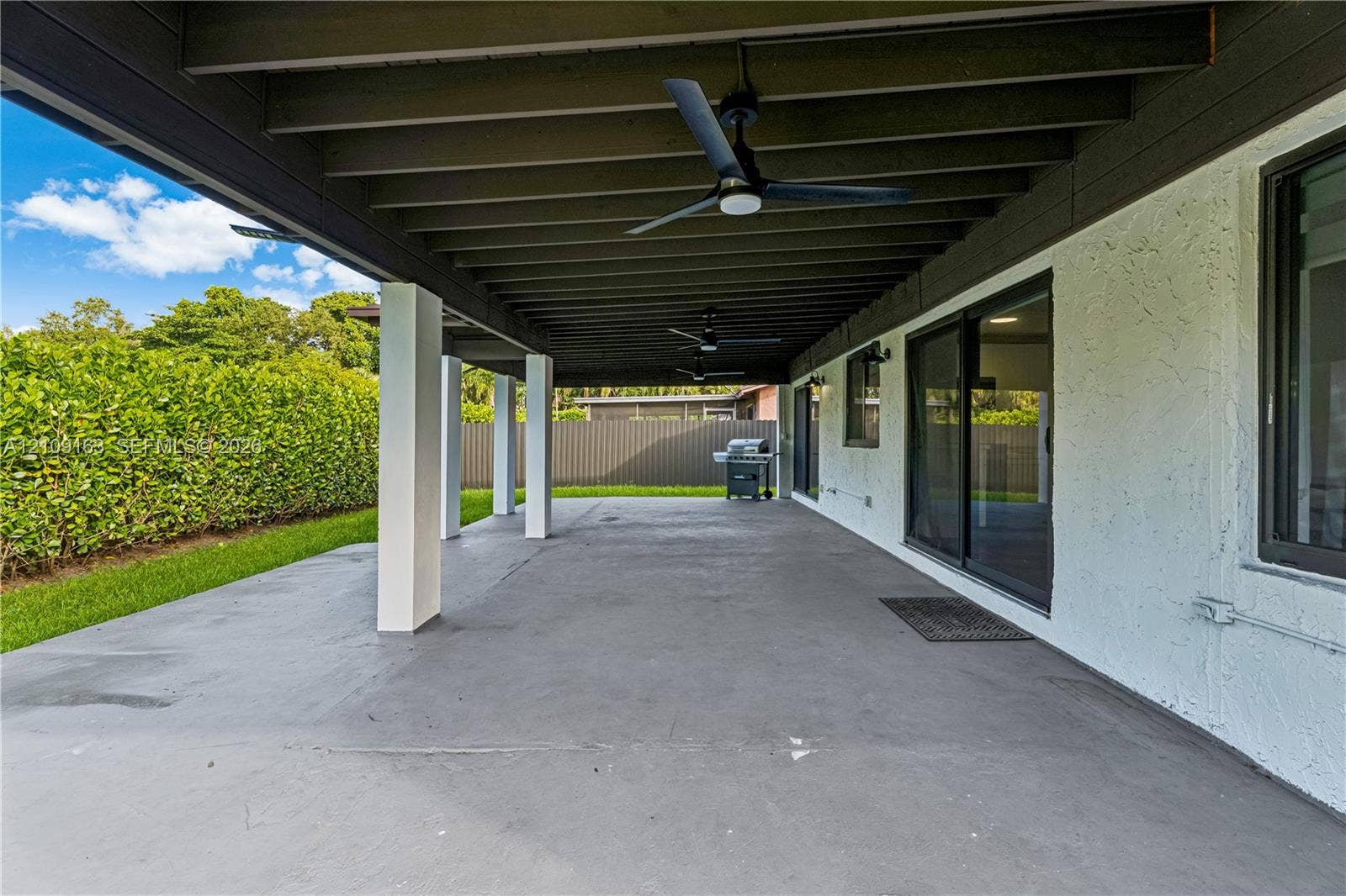 9122 SW 127th Avenue, Miami, FL 33186 Covered outdoor patio featuring a painted concrete floor, exposed beam ceiling, multiple mounted ceiling fans, and sliding glass door access