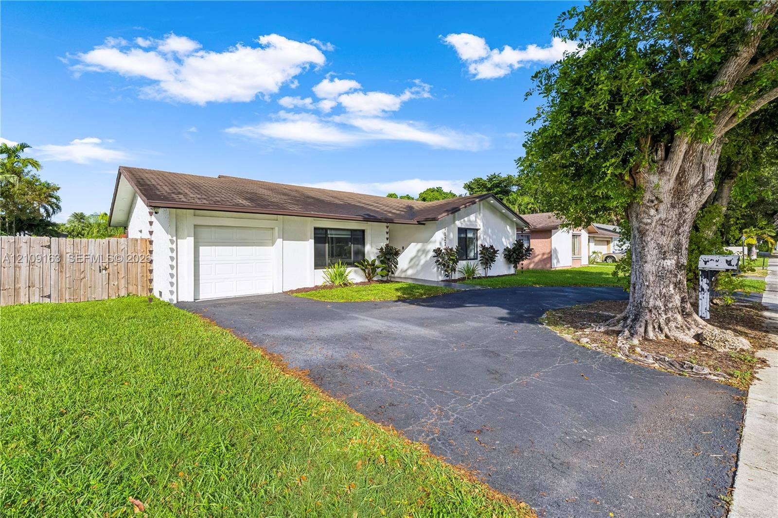9122 SW 127th Avenue, Miami, FL 33186 Single-story exterior featuring white stucco siding, a low-pitch roof, an attached one-car garage, asphalt driveway, and a wood-panel fence