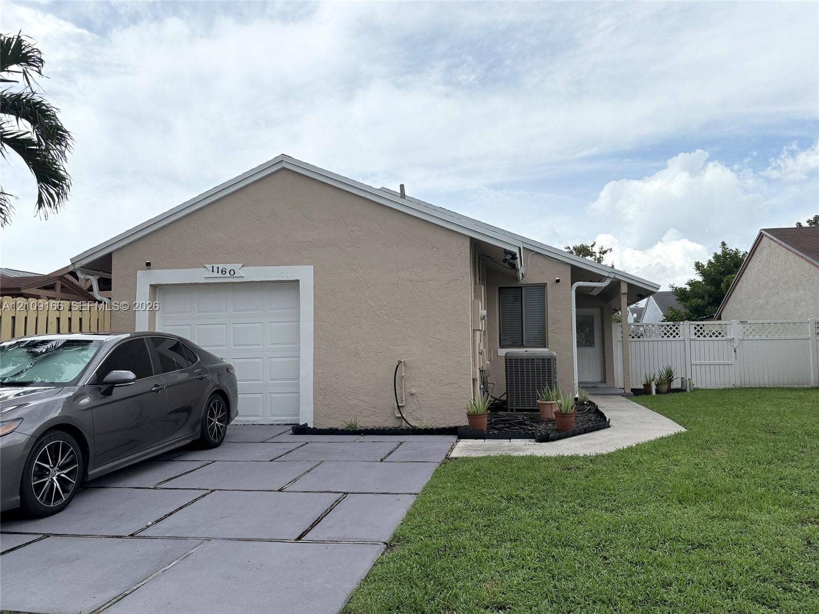 Single-story exterior featuring a textured stucco finish, concrete slab driveway, one-car garage, and perimeter lattice-topped privacy fencing