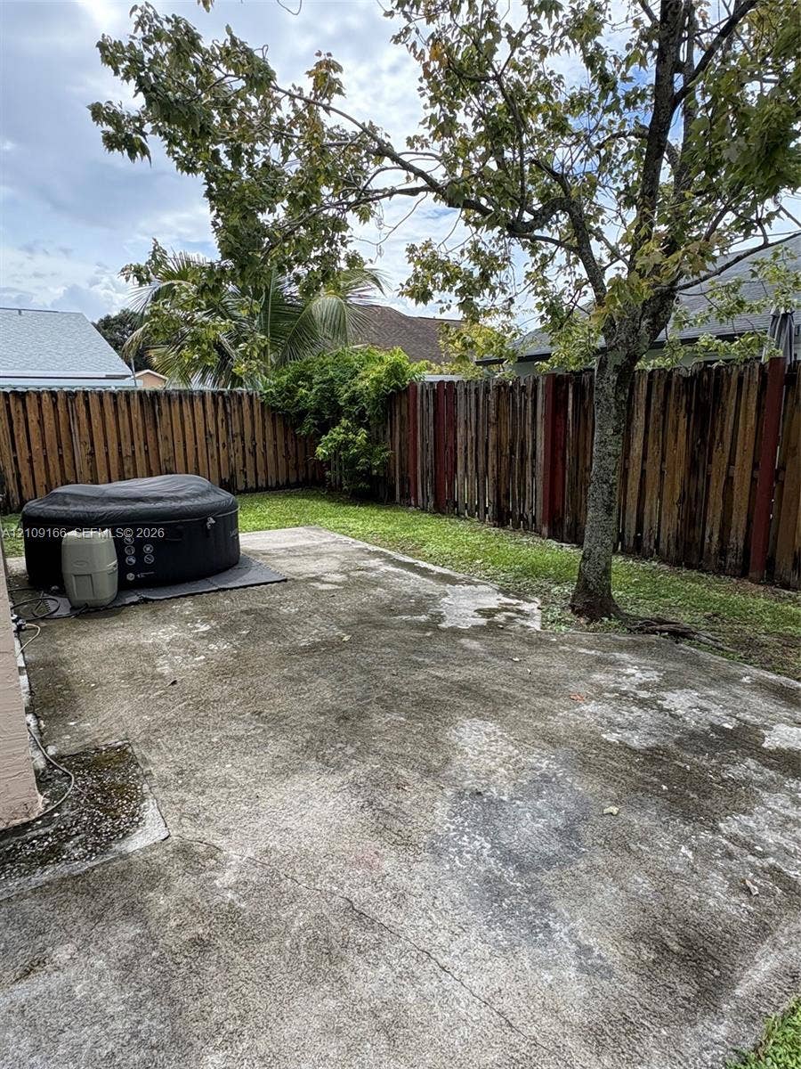 Rear exterior space featuring a concrete patio, wood privacy fencing, and a mature tree
