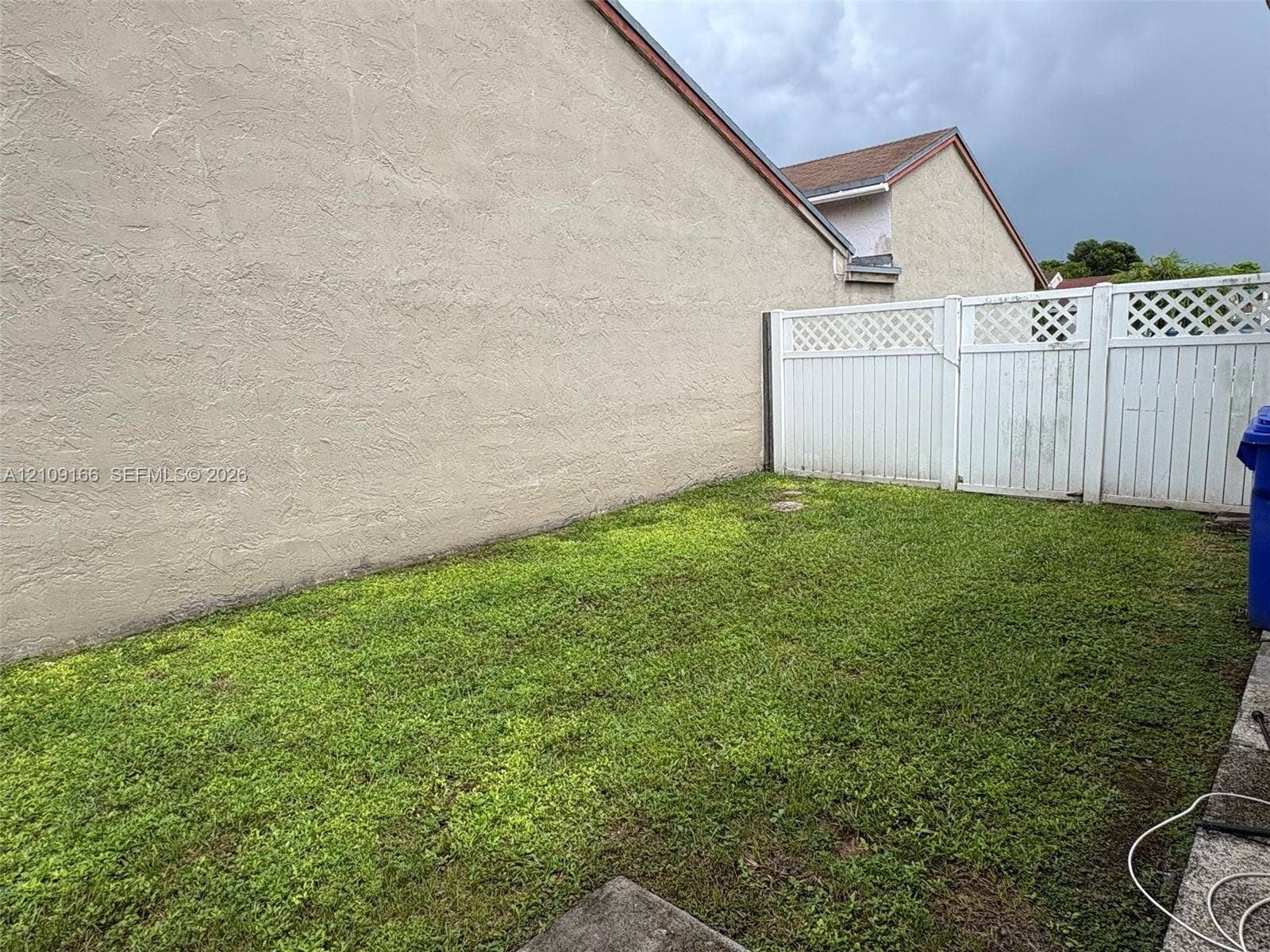 Rear yard featuring a grass lawn, stucco exterior wall, and white vinyl privacy fencing with lattice detail