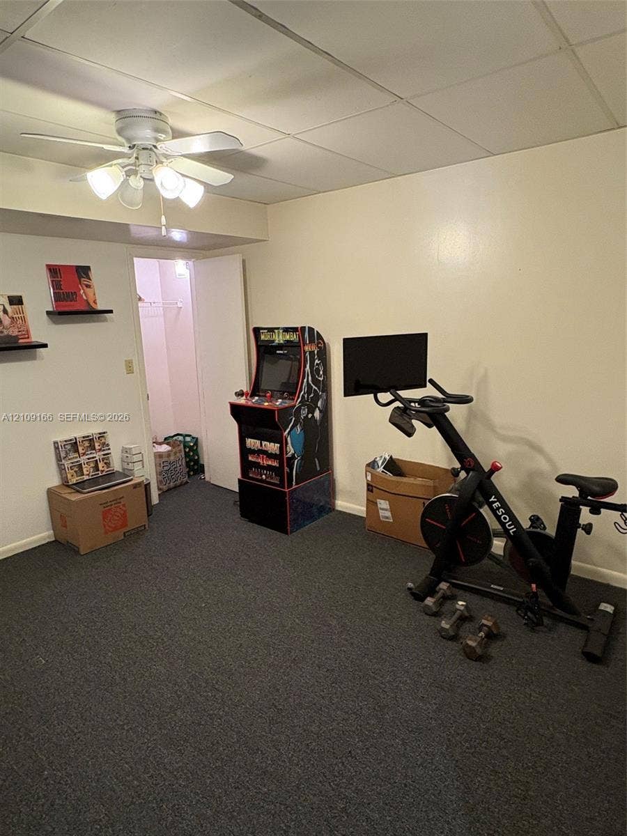 Neutral-toned interior space featuring dark wall-to-wall carpeting, a drop ceiling, a ceiling-mounted light fixture with four glass shades, and an enclosed storage closet