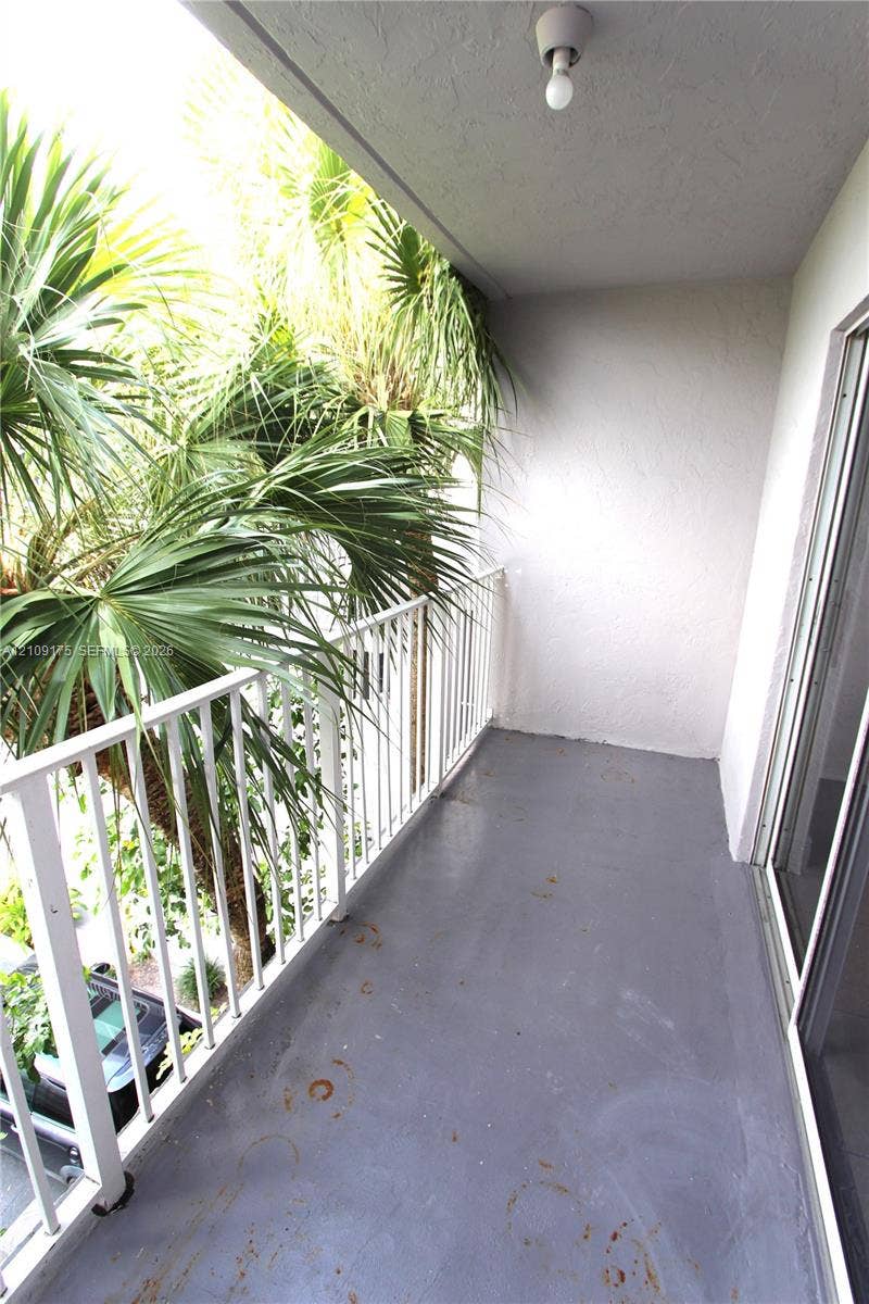 Covered balcony featuring concrete flooring, a white metal railing, and ceiling-mounted light fixture