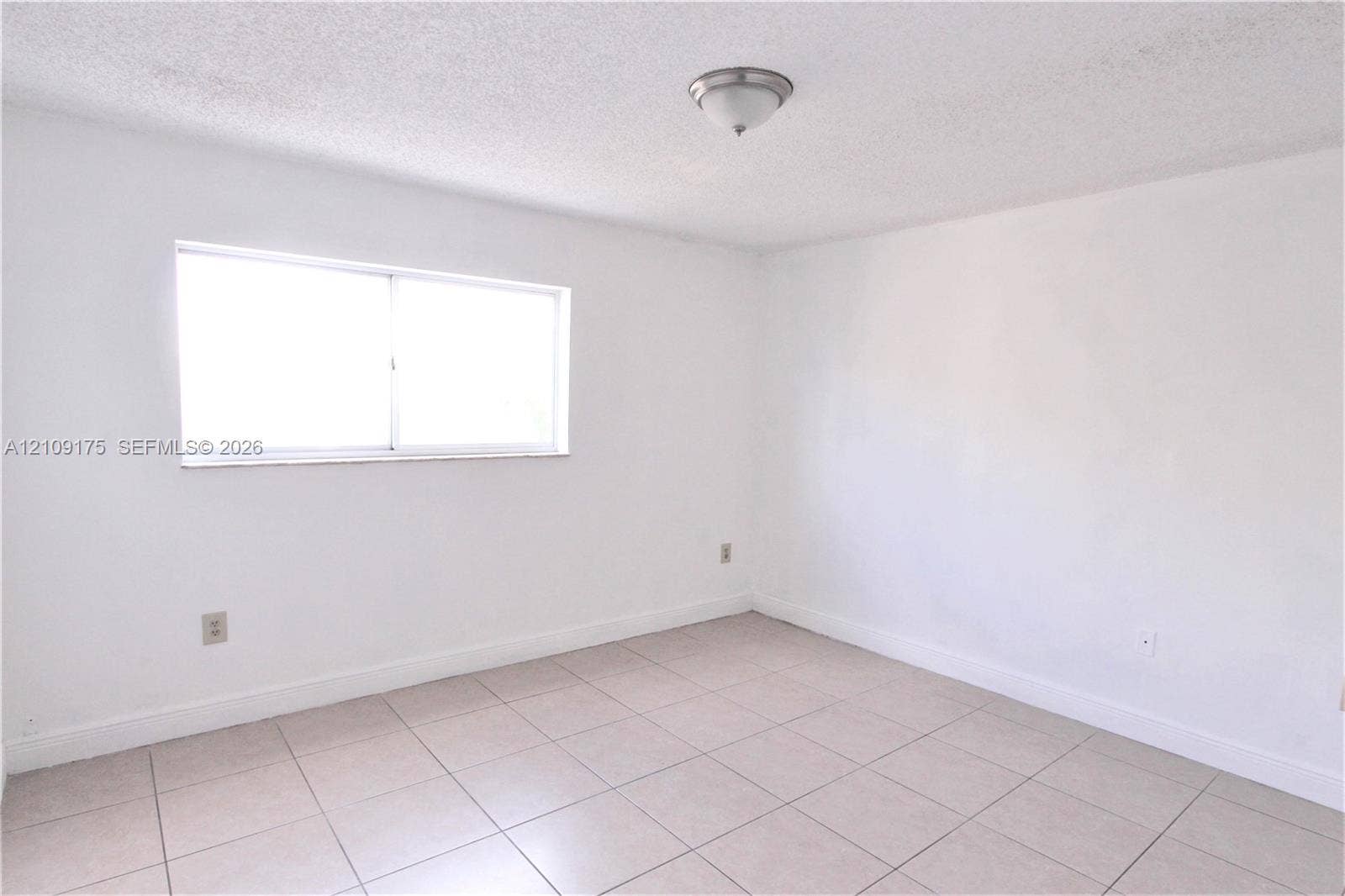 Room with large-format light-toned tile flooring, neutral wall finishes, single-pane sliding window, and ceiling-mounted dome light fixture