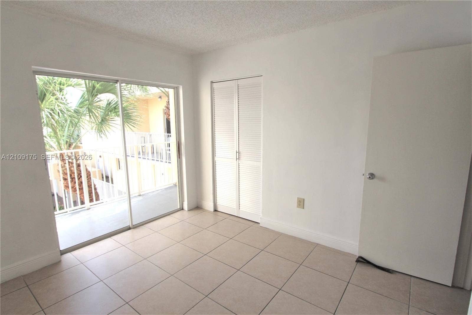 Neutral-toned floor tiles, sliding glass balcony doors, and built-in closet with louvered doors