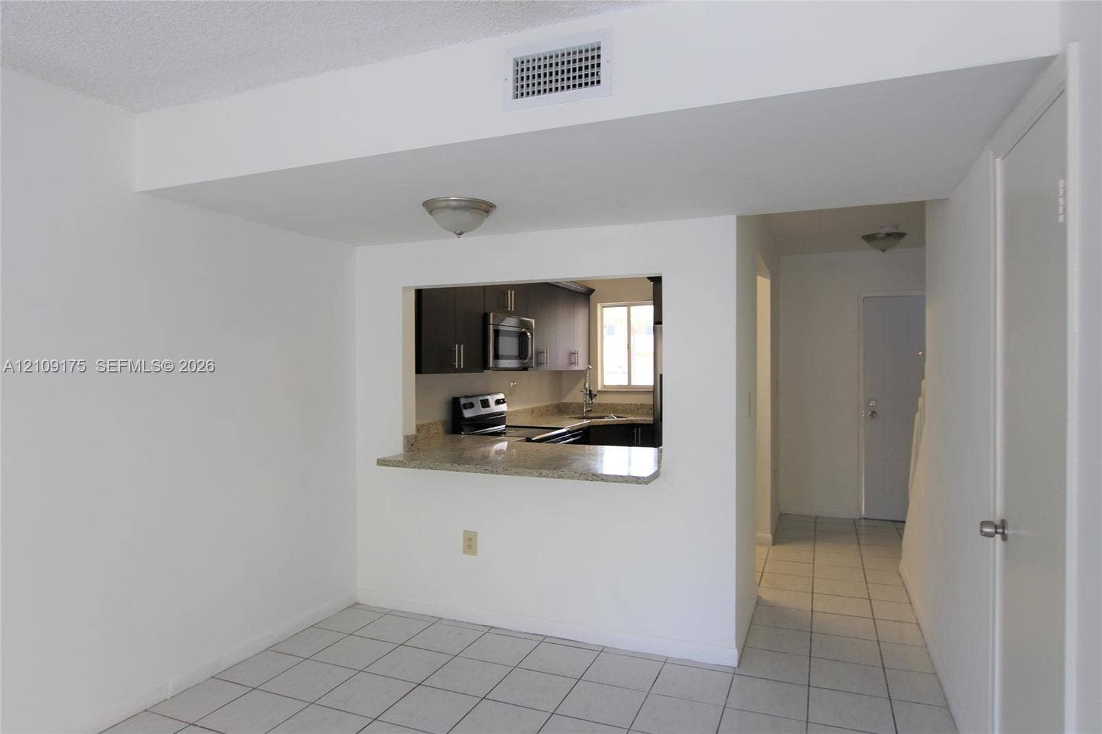 Kitchen featuring dark cabinetry, stone-surface countertop with bar seating, and stainless steel microwave