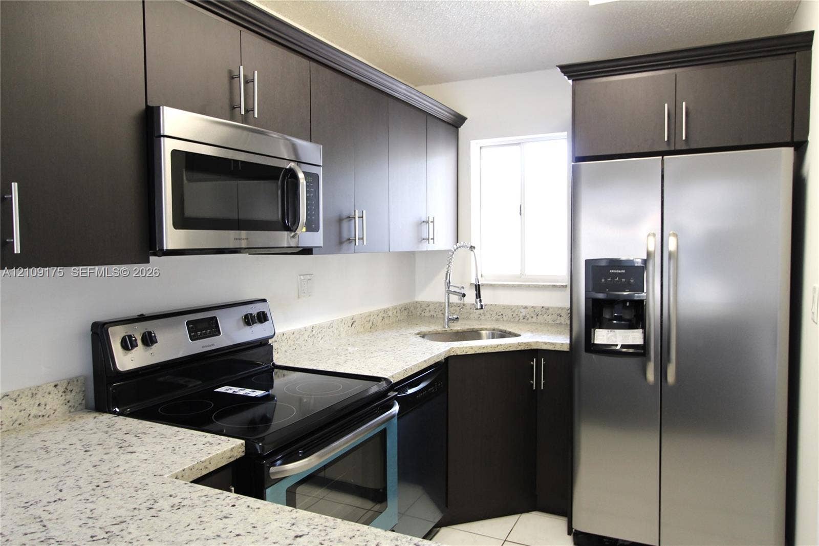 Kitchen featuring dark-toned cabinetry, stainless steel appliances, stone-patterned countertops, a stainless steel gooseneck faucet, and a dual-basin sink