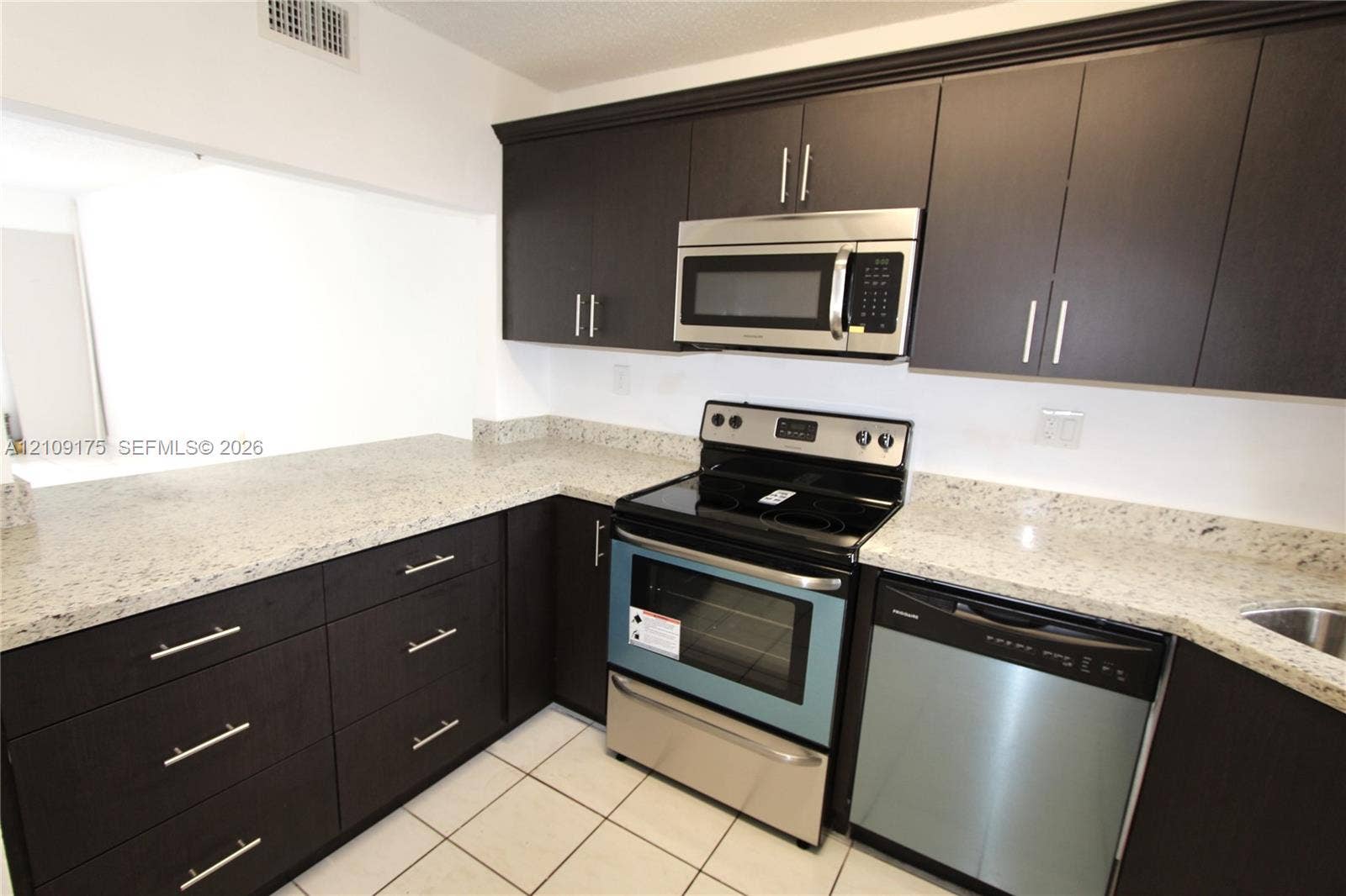 Kitchen featuring dark cabinetry, stone-finish countertops, stainless steel appliances, and ceramic tile flooring