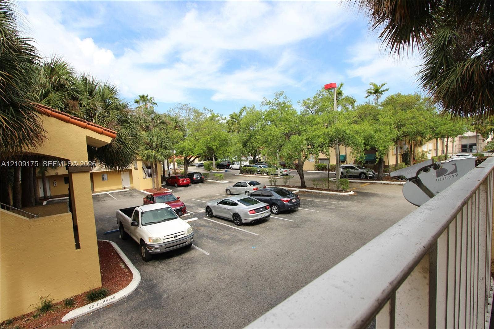 Paved parking lot featuring lined spaces, stucco exterior walls, and mature landscaping