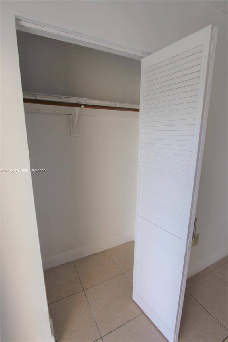 Storage closet featuring a white louvered door and a built-in shelf with a hanging rod