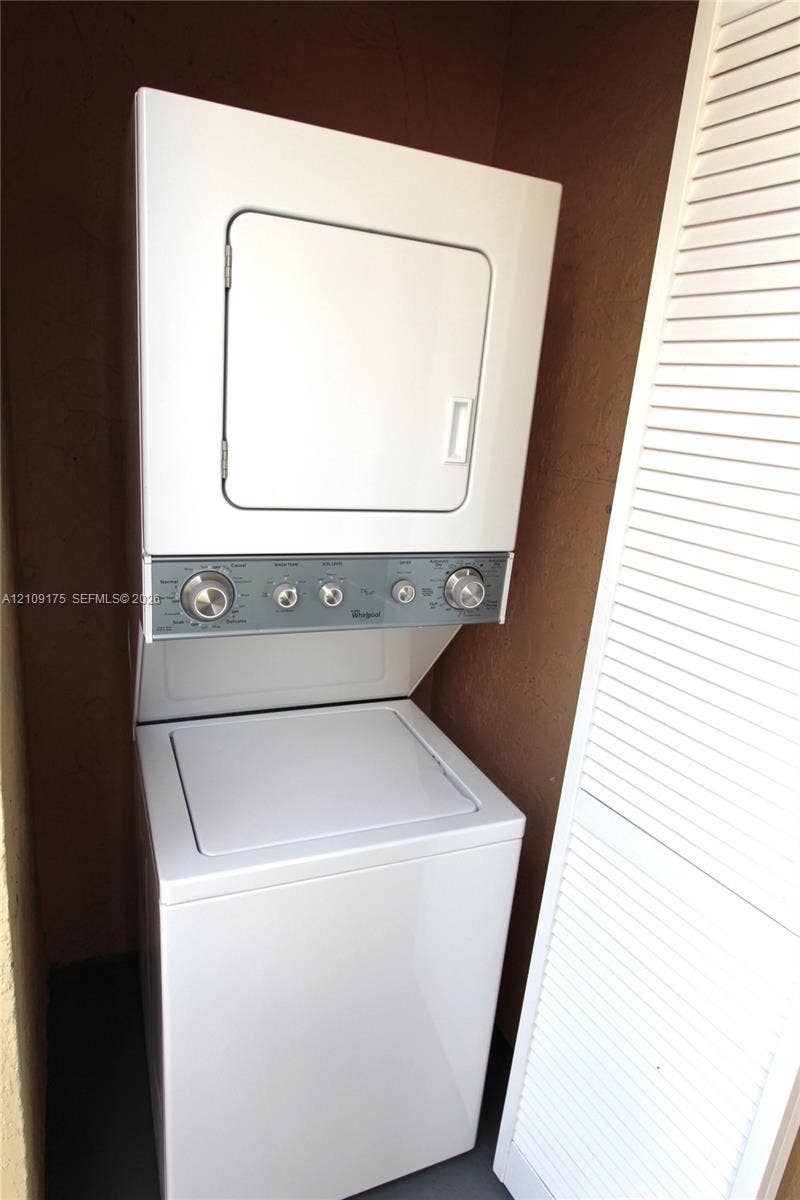 Stacked white washer and dryer unit with a top-loading basin and white louvered enclosure doors