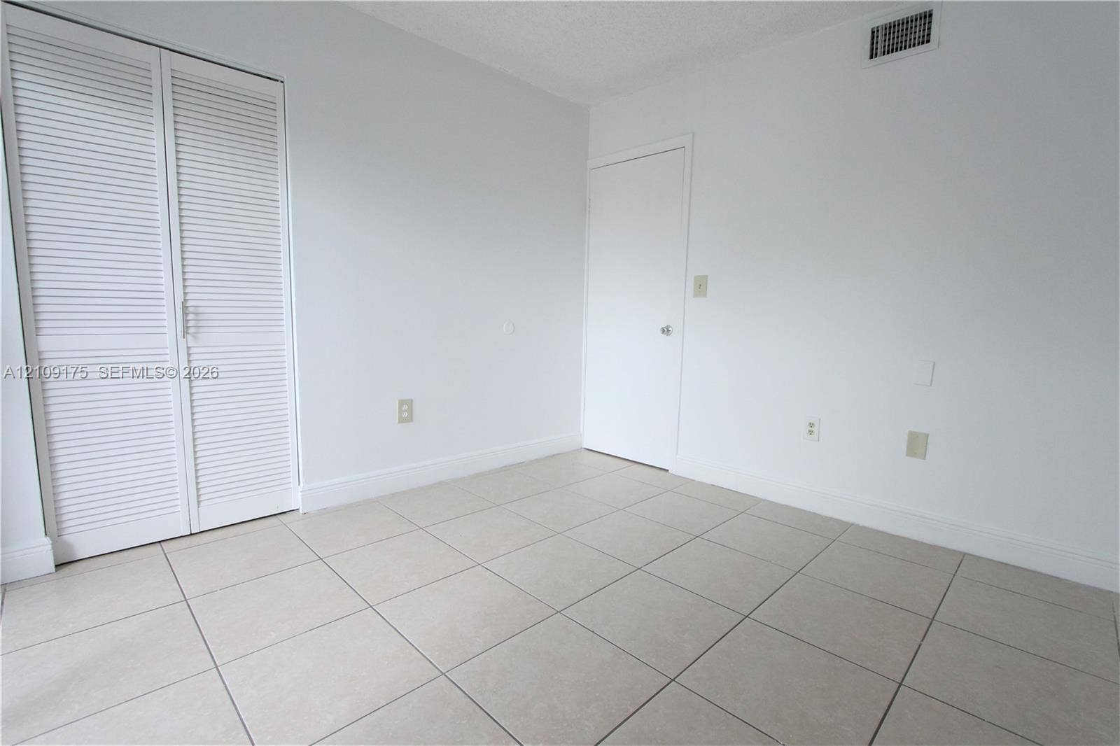 Neutral-toned tile flooring, white louvered-door closet, and solid core interior door