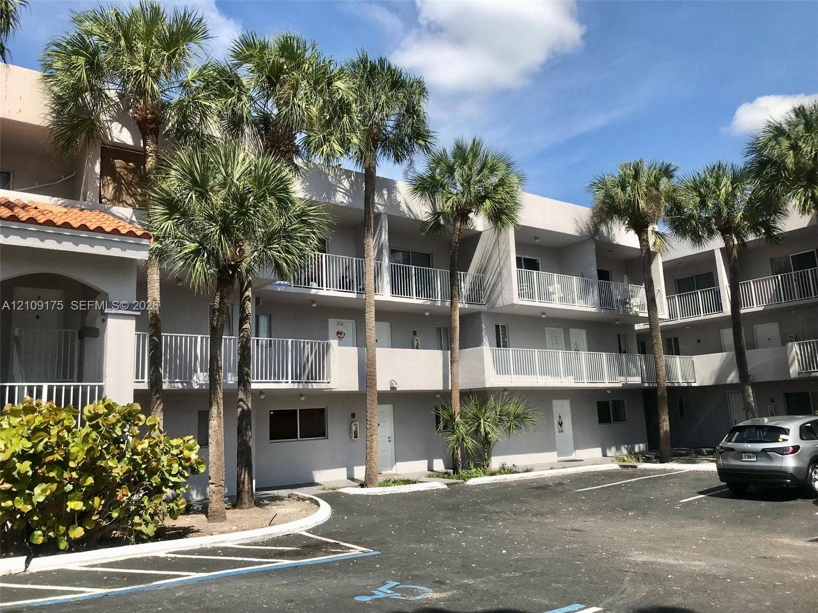 Multi-story exterior featuring a neutral stucco facade, private balconies with white railings, and mature palm landscaping