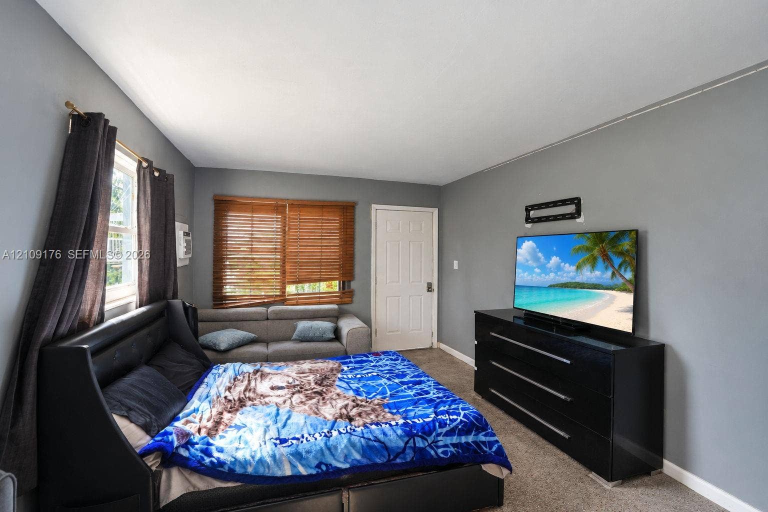 Room featuring neutral wall paint, carpeting, a solid-core paneled entry door, and window blinds