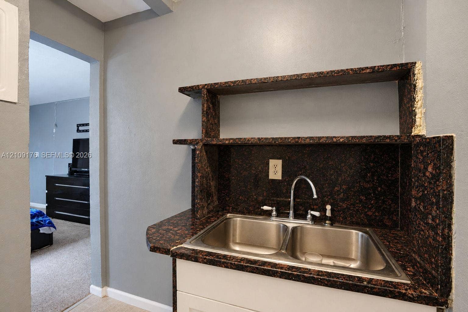 Built-in wet bar featuring stone-finish countertop, dual-basin stainless steel sink, chrome faucet, and integrated shelving