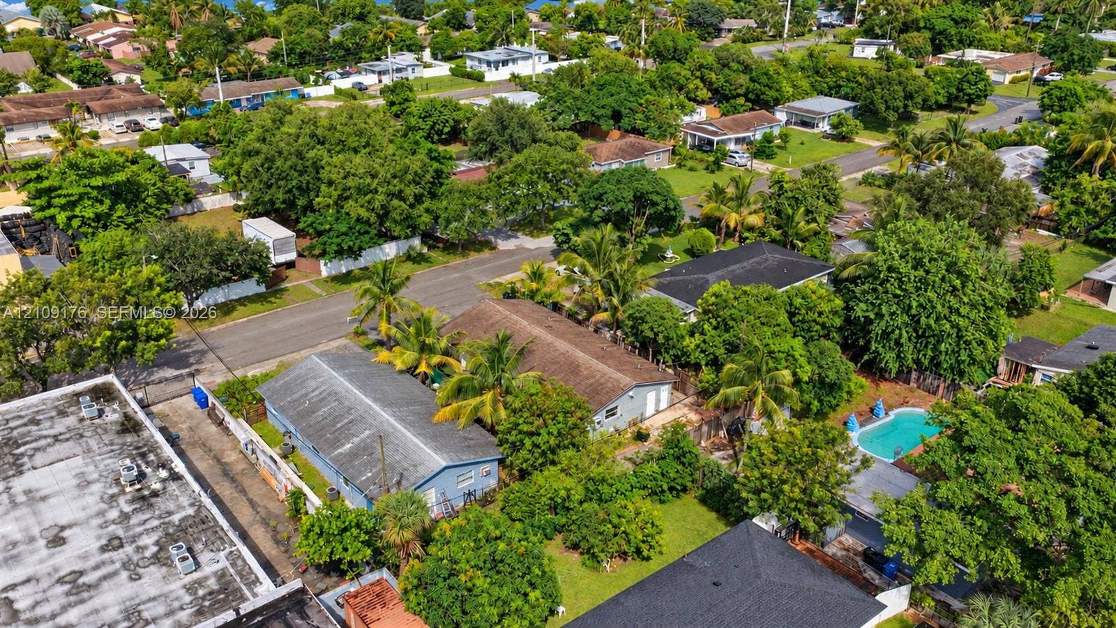 Aerial perspective featuring residential structures, mature tropical trees, and a private swimming pool