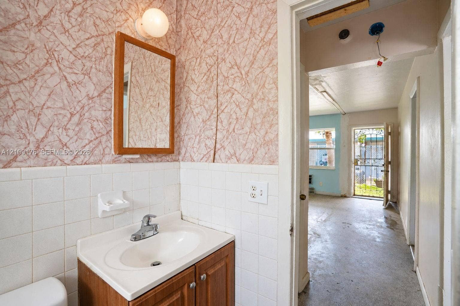 Bathroom featuring a wood-toned vanity cabinet, integrated sink with a metal faucet, wall-mounted light fixture, and tiled backsplash
