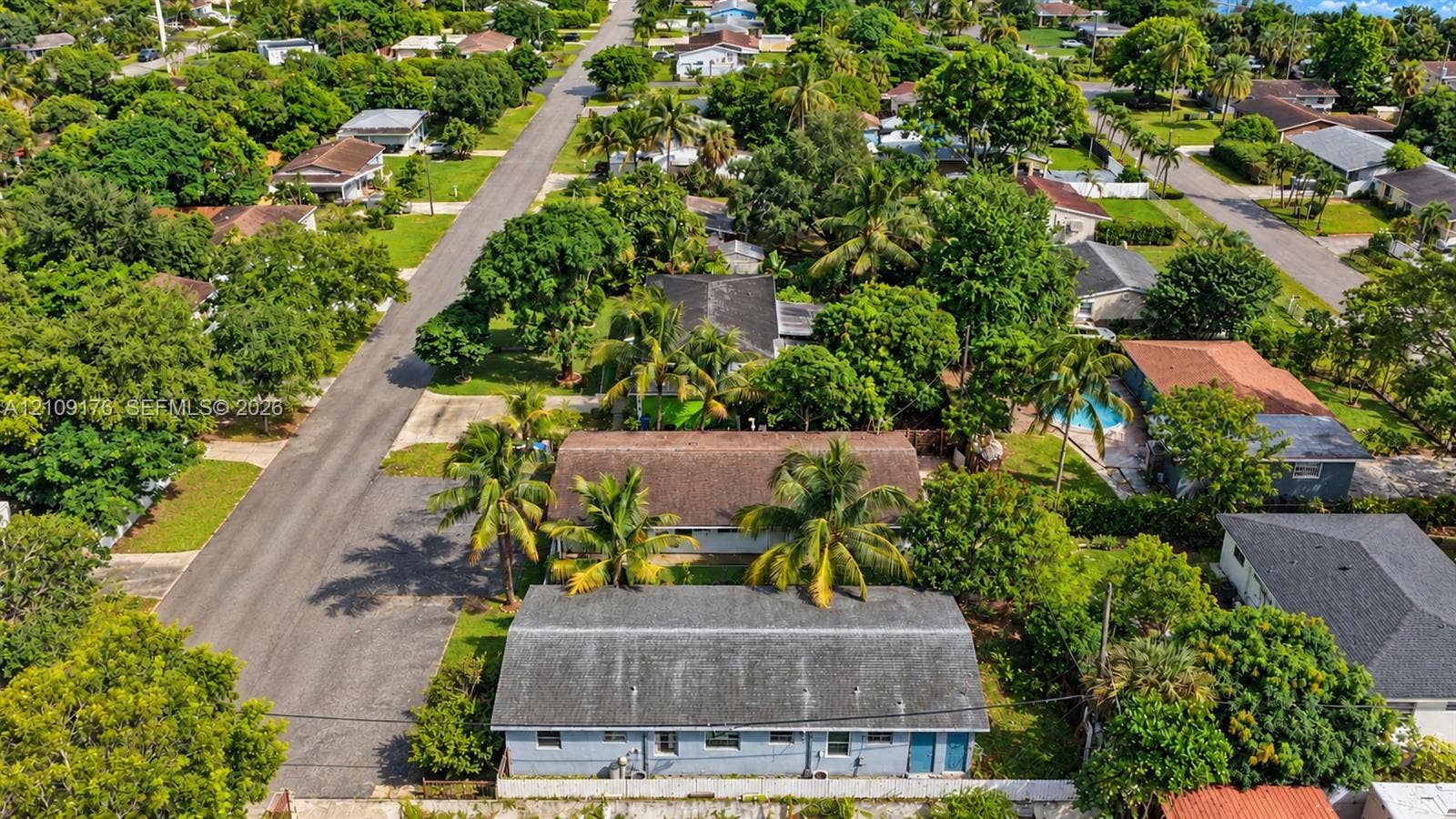 Aerial perspective of a single-story residence featuring a shingled roof, light-toned exterior finish, and mature palm trees within a landscaped residential setting