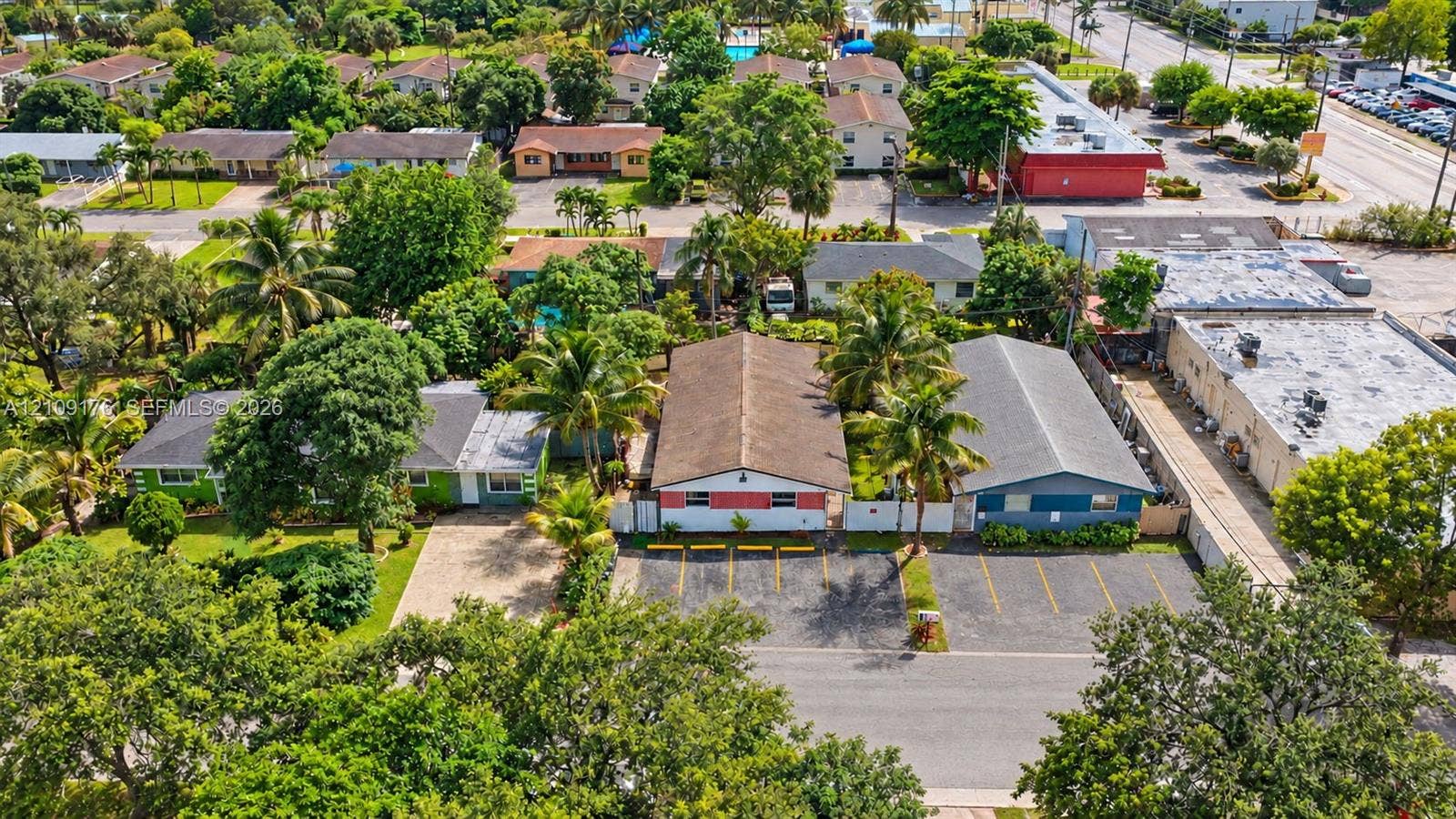 Aerial perspective of property featuring paved off-street parking, mature landscaping, and pitched shingle roofing