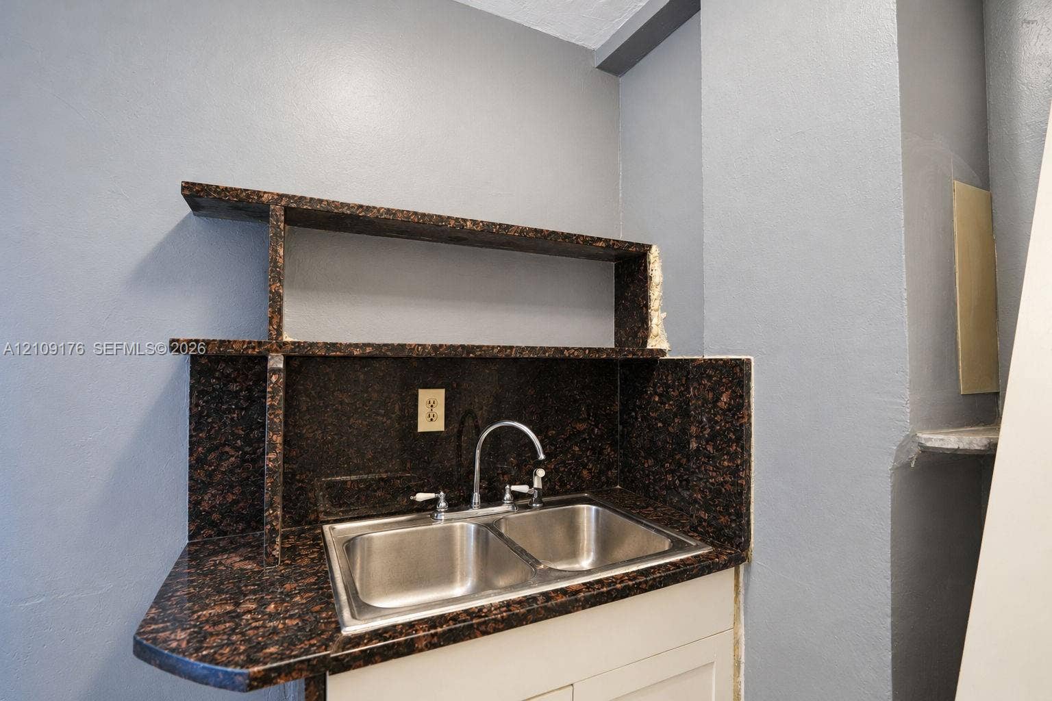 Built-in stone-surface shelving with matching backsplash and dual-basin stainless steel sink featuring a gooseneck faucet