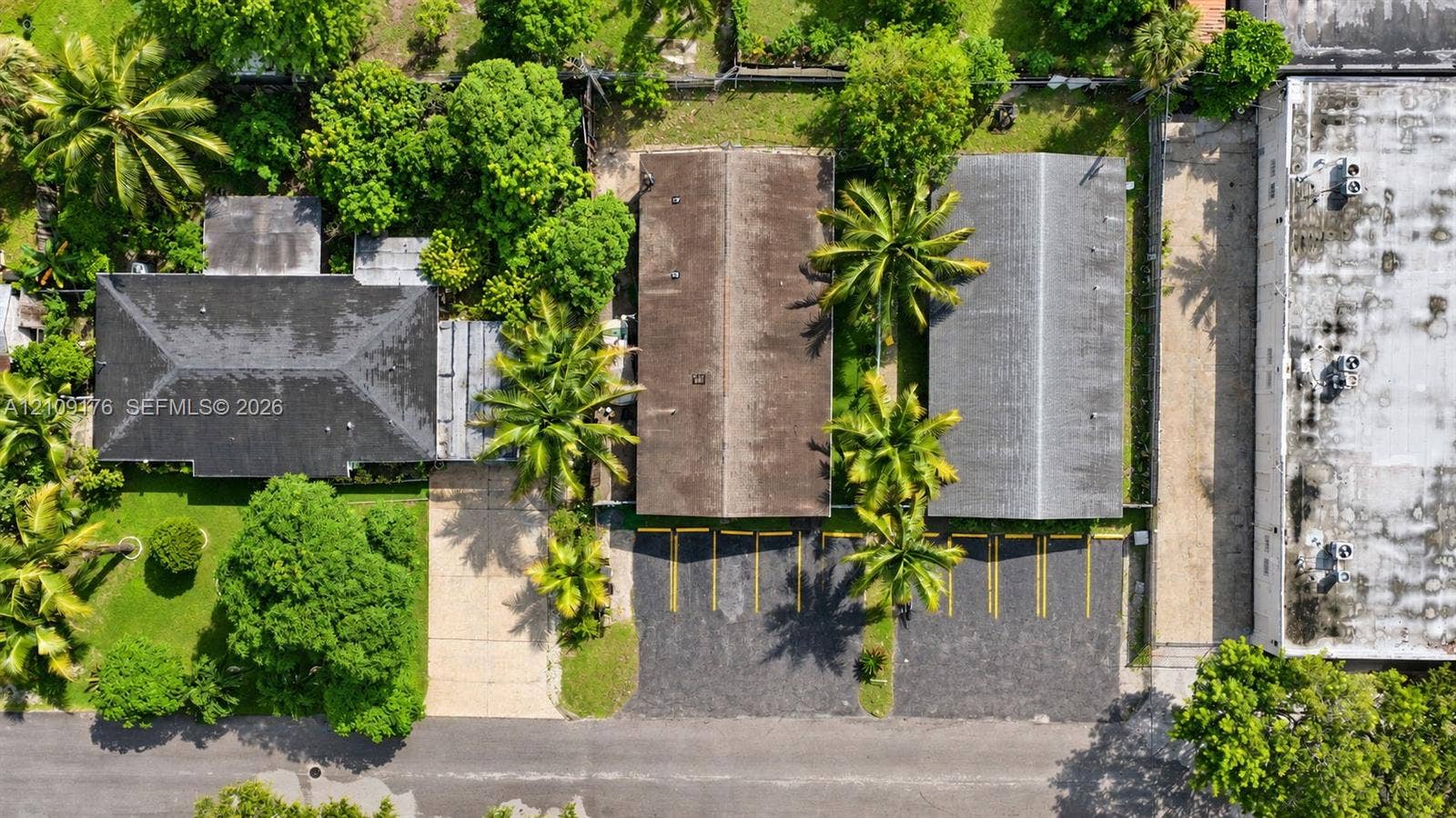 Aerial perspective featuring multiple structures, dedicated paved parking area with striped stalls, and mature trees situated on the property grounds
