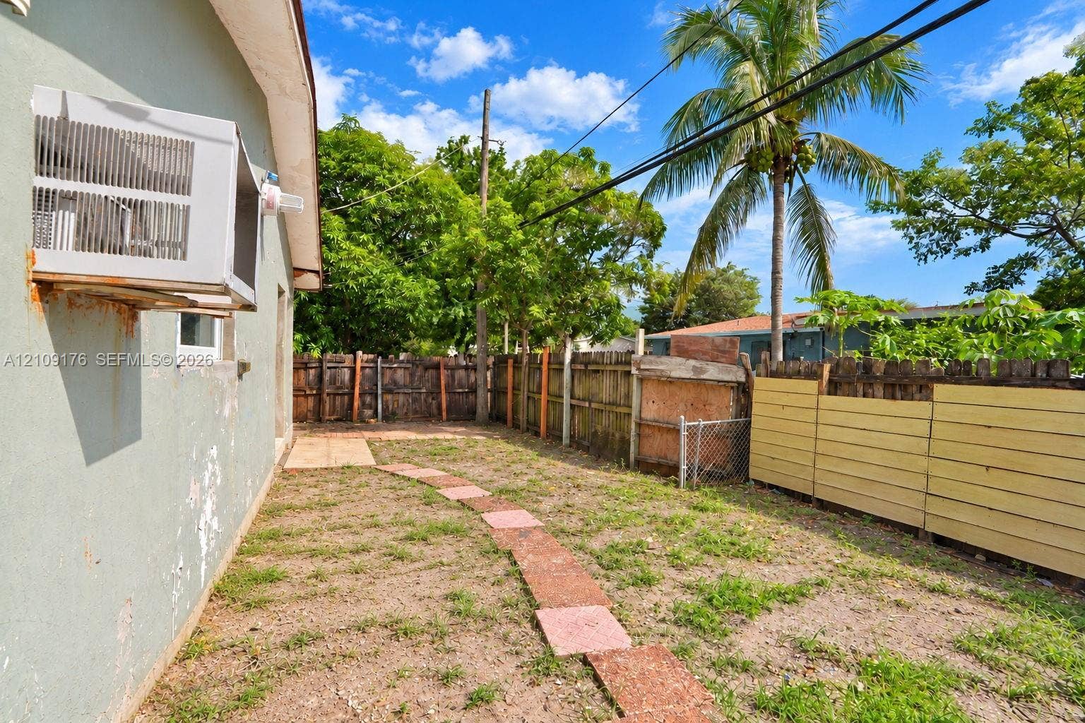 Exterior side yard featuring a concrete paver path, wood fencing, and mature palm trees