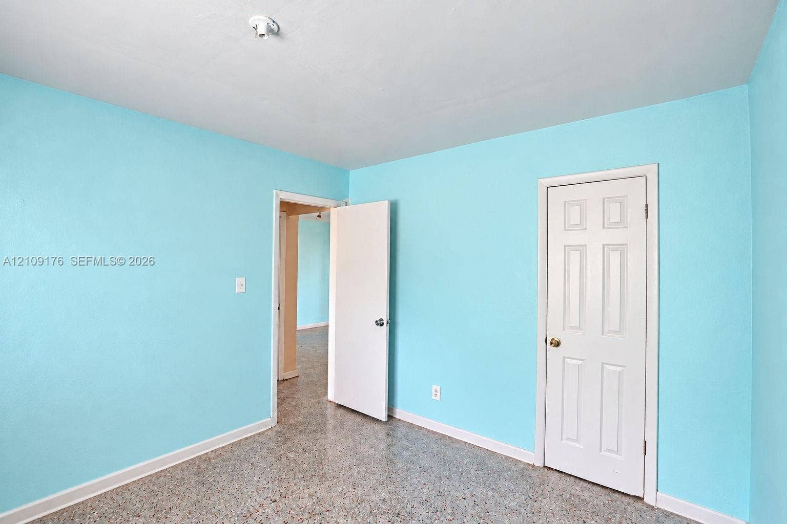 Interior room featuring terrazzo flooring, six-panel interior door, and flush-mount lighting