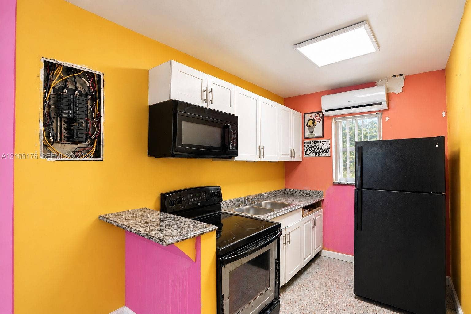 Kitchen featuring white cabinetry, stone-finish countertops, stainless steel sink, black range with over-the-range microwave, and wall-mounted climate control unit