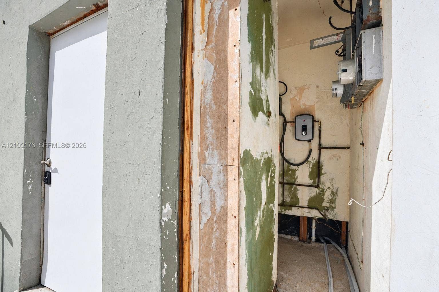 Utility alcove featuring an exterior door, exposed structural framing, wall-mounted electrical panel, and tankless water heater