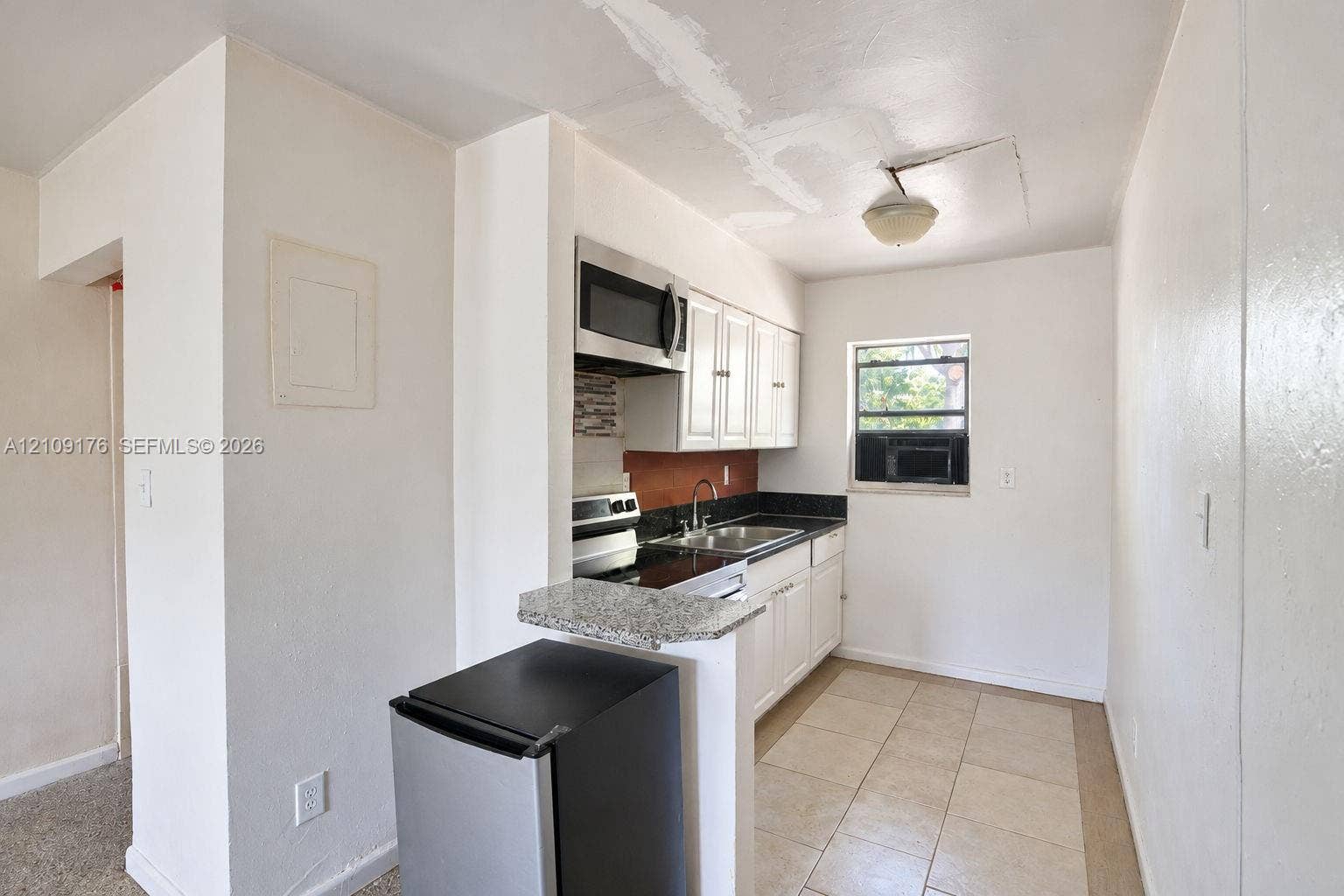 Kitchen featuring white cabinetry, stone-finish countertops, stainless steel microwave, metal sink, and tiled flooring