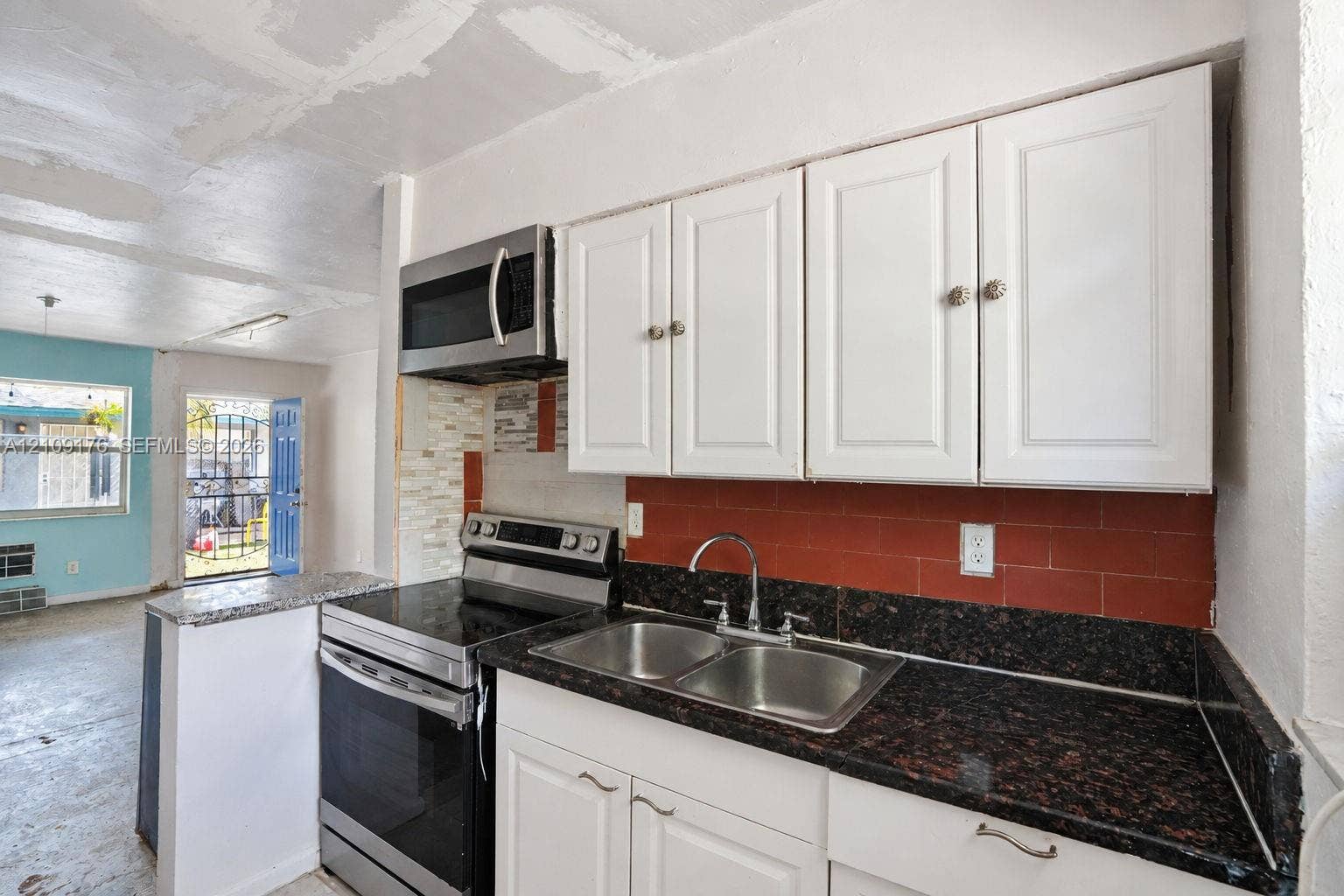 Kitchen featuring white cabinetry, dark stone-finish countertops, dual-basin stainless steel sink with a high-arch faucet, and stainless steel appliances