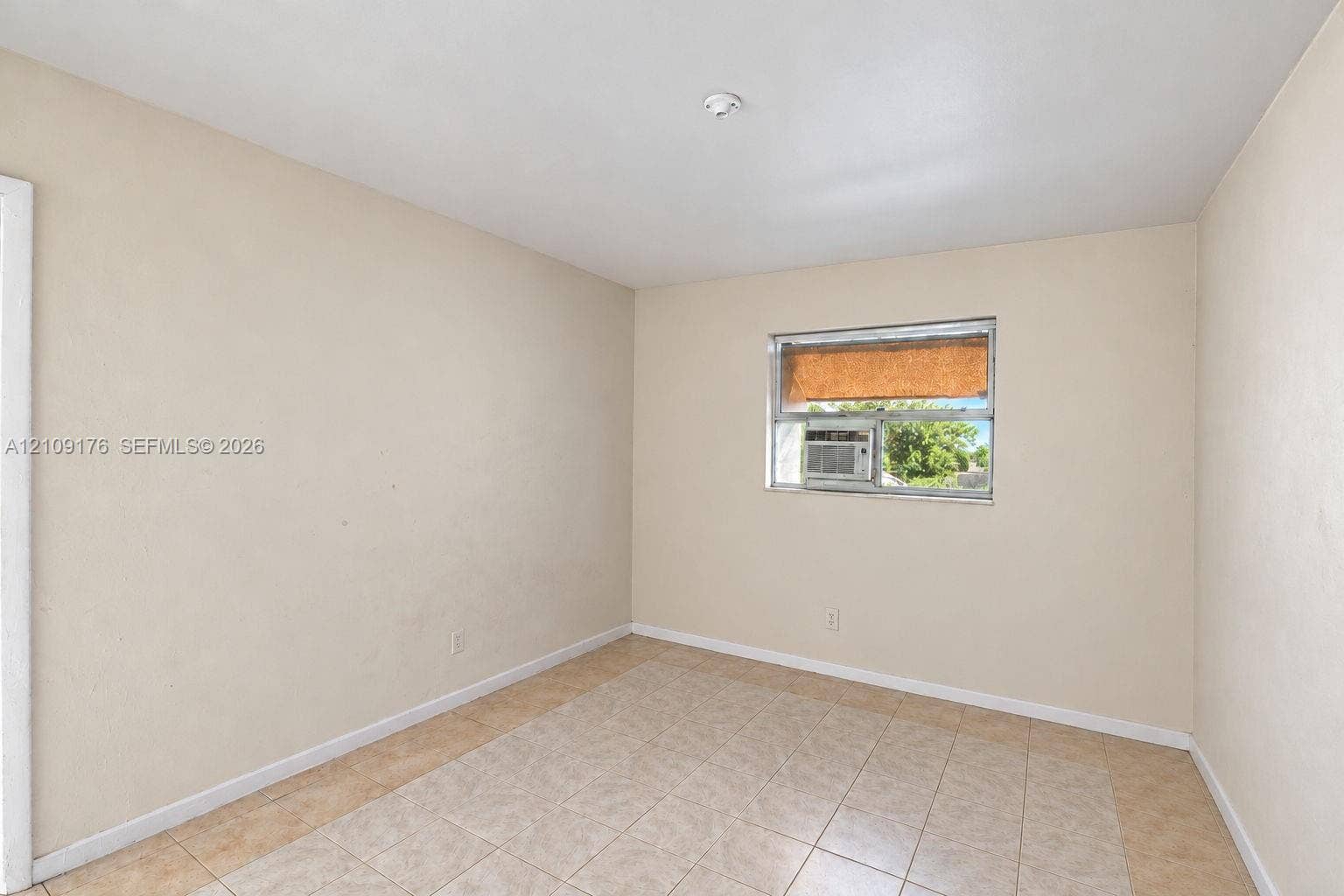 Interior space featuring neutral wall tones, large-format tile flooring, and a window with a built-in air conditioning unit
