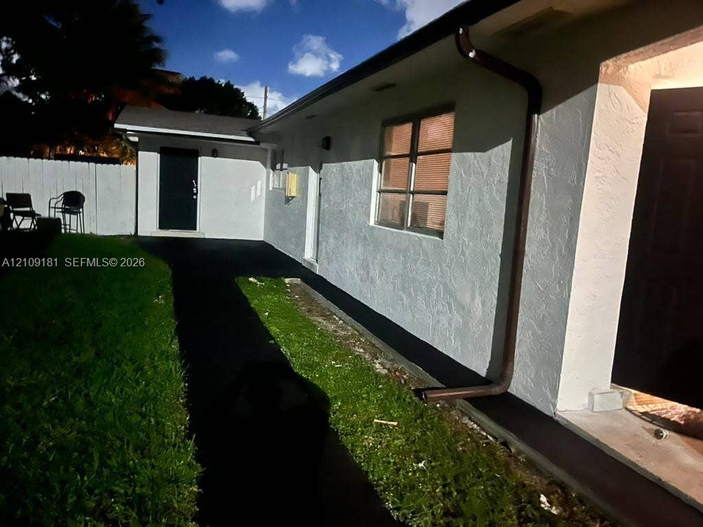 727 SW 10th Street, #1, Hallandale Beach, Hallandale Beach, FL 33009 Exterior featuring a white stucco facade, paved walkway, and white privacy fencing
