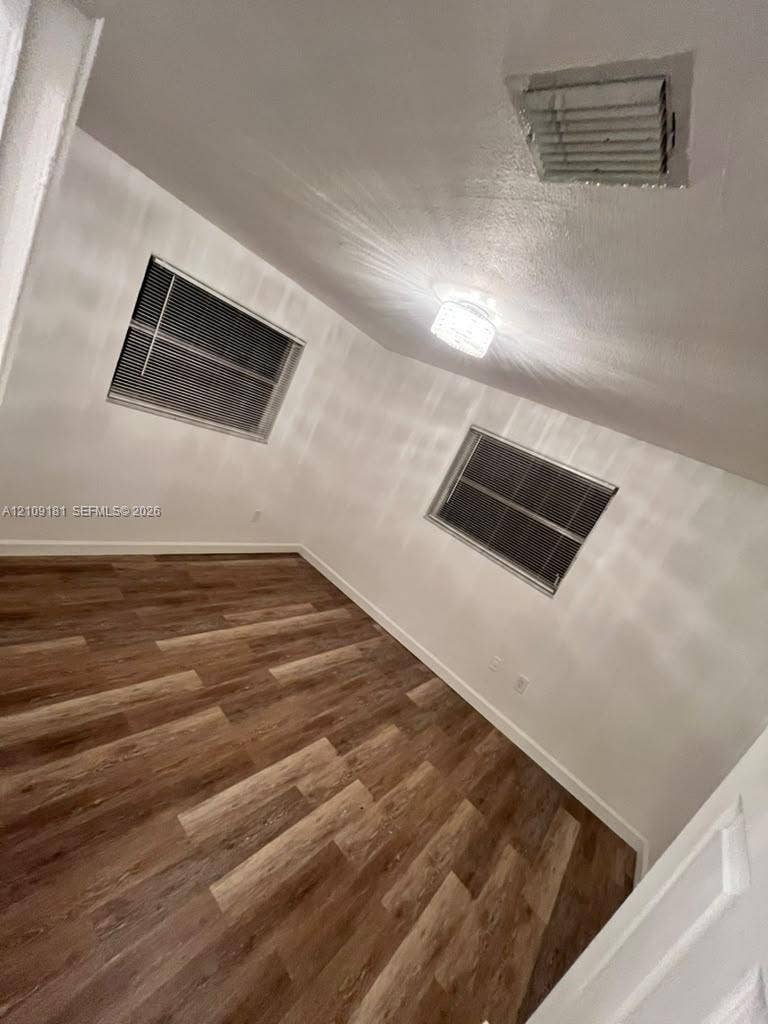 727 SW 10th Street, #1, Hallandale Beach, Hallandale Beach, FL 33009 Interior room featuring wood-finish flooring, white walls, two windows with horizontal blinds, and a crystal-style flush mount ceiling light