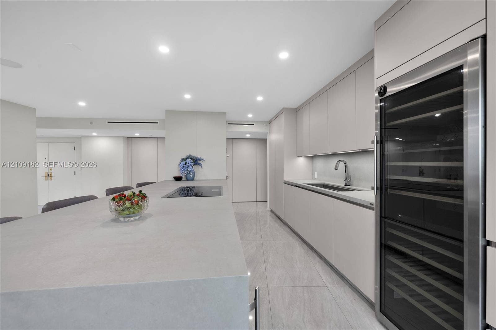 Contemporary kitchen featuring flat-panel cabinetry, a stone-finish waterfall edge island, a built-in wine refrigerator, integrated cooktop, and neutral large-format tile flooring