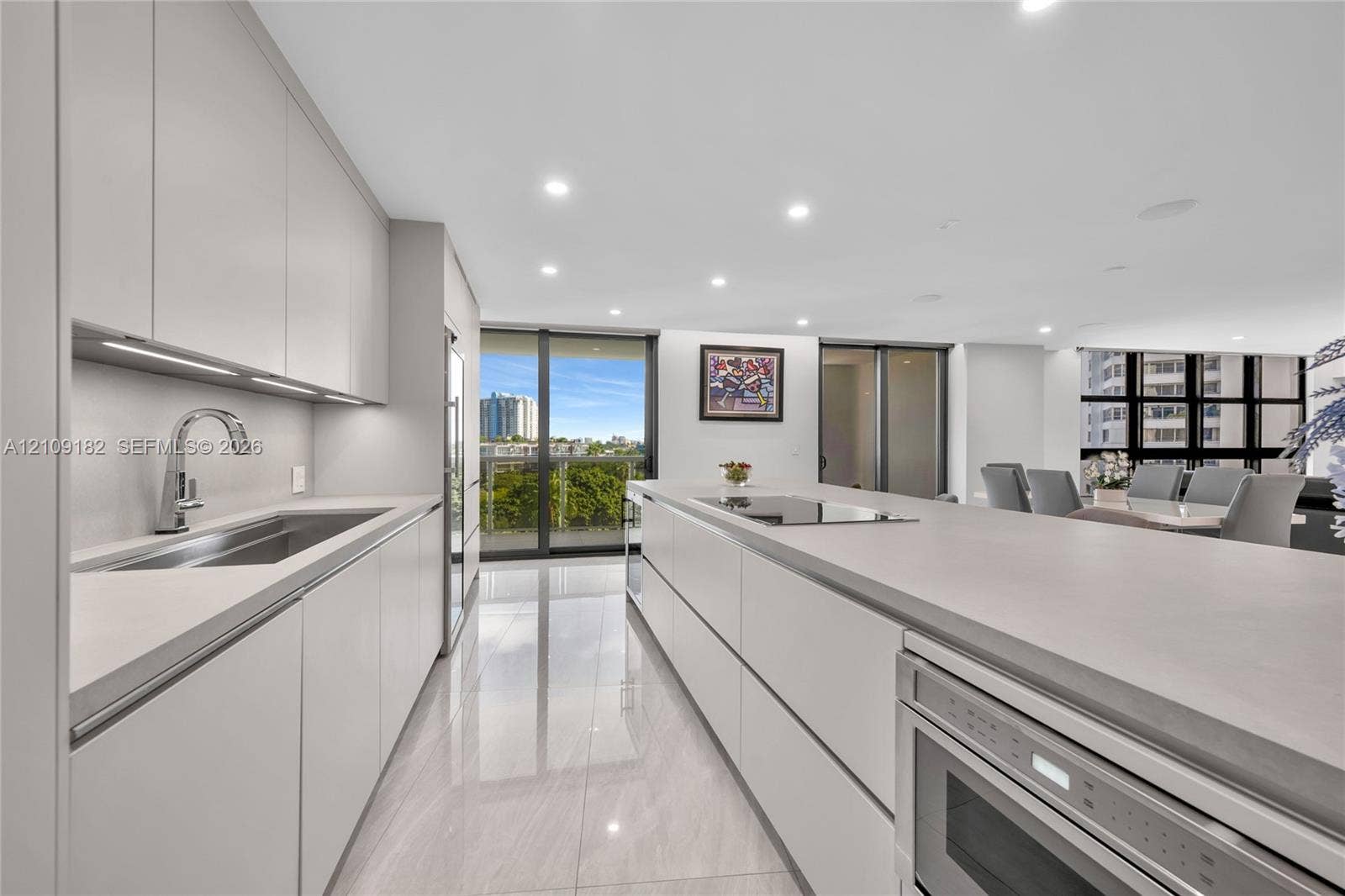 Modern kitchen featuring sleek flat-panel cabinetry, a spacious island with an integrated cooktop, stone-finish countertops, tile flooring, and recessed ceiling lighting