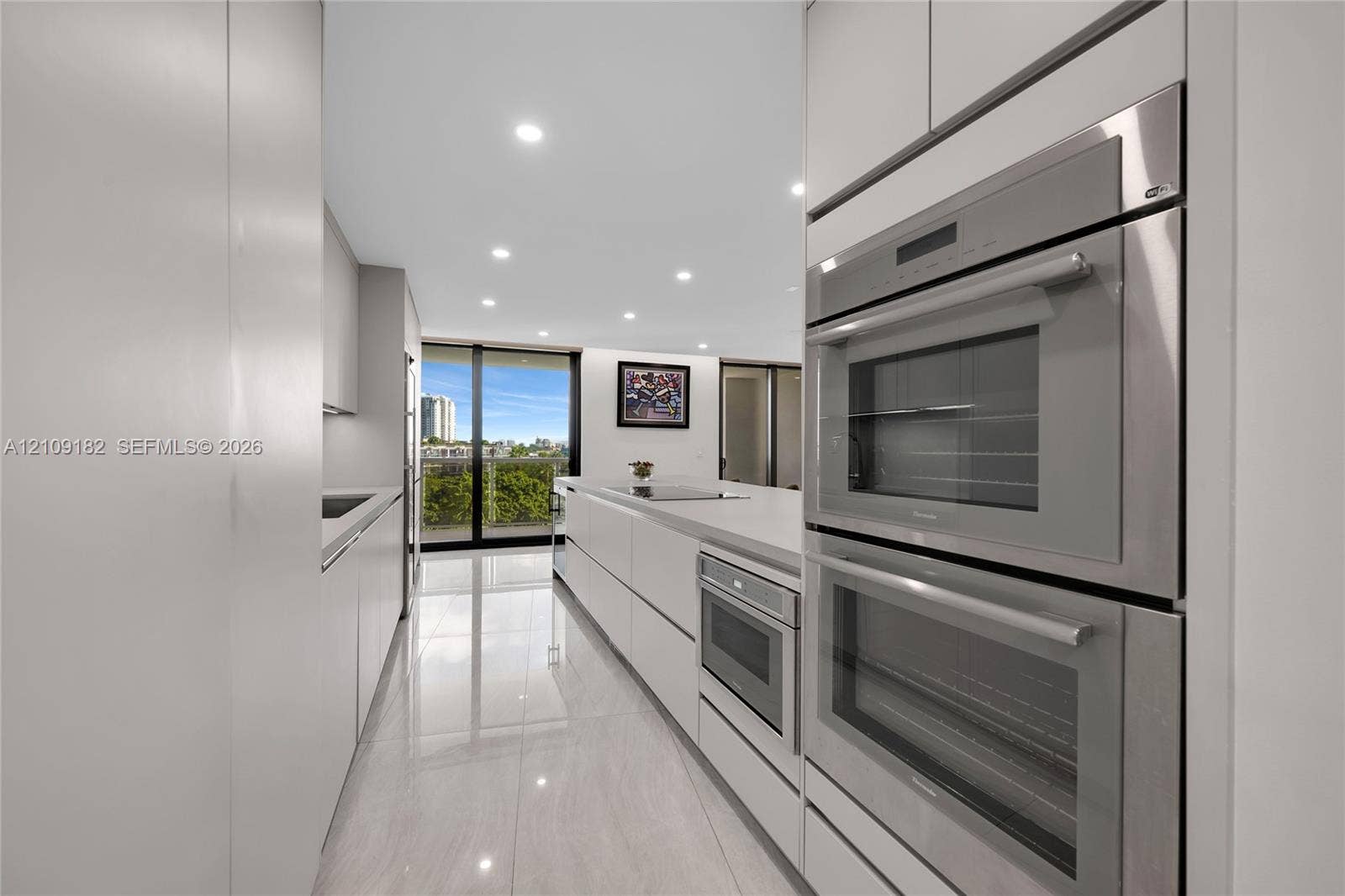 Contemporary kitchen featuring handleless cabinetry, integrated stainless steel double ovens, a built-in microwave, stone countertops, and polished tile flooring