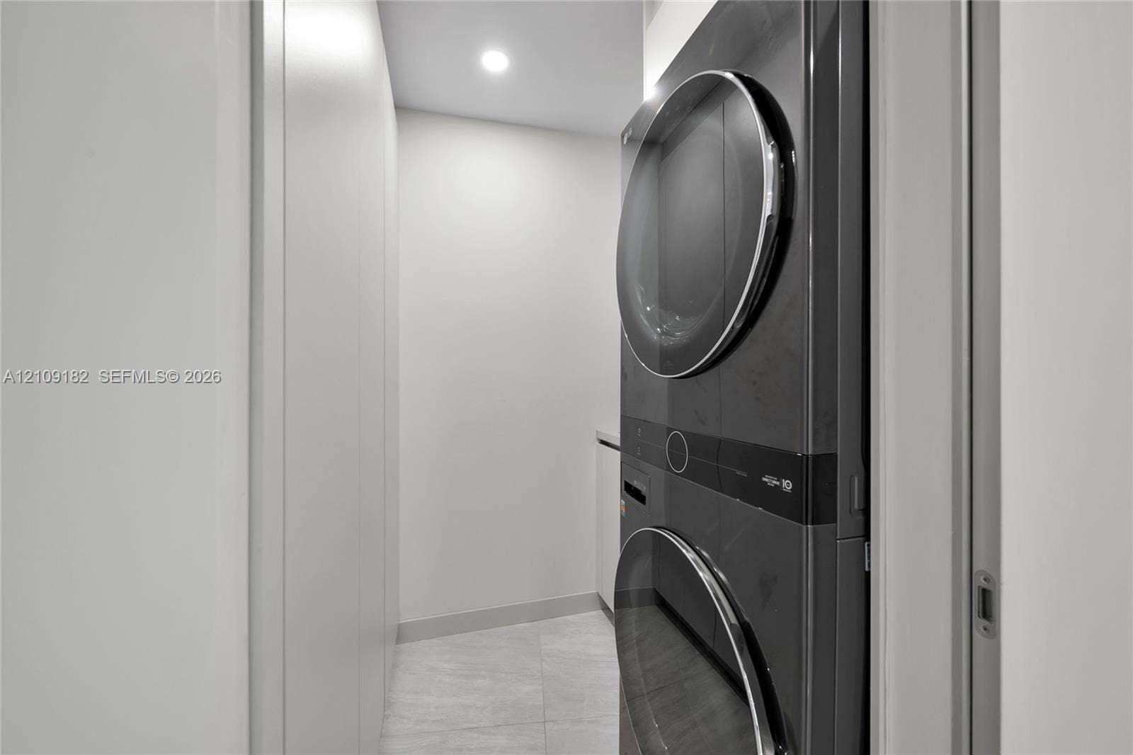 Stacked charcoal-toned laundry unit with recessed lighting, integrated cabinetry, and stone-finish tile flooring