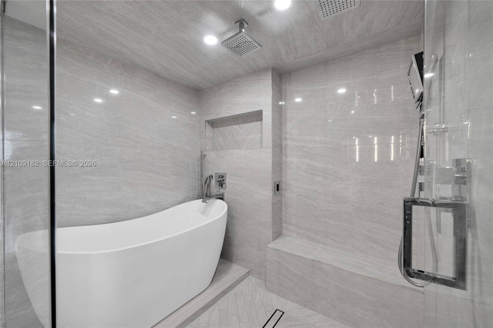 Freestanding soaking tub, floor-to-ceiling stone-finish tile surround, built-in recessed shower niche, integrated stone bench, and glass-enclosed shower featuring dual showerheads