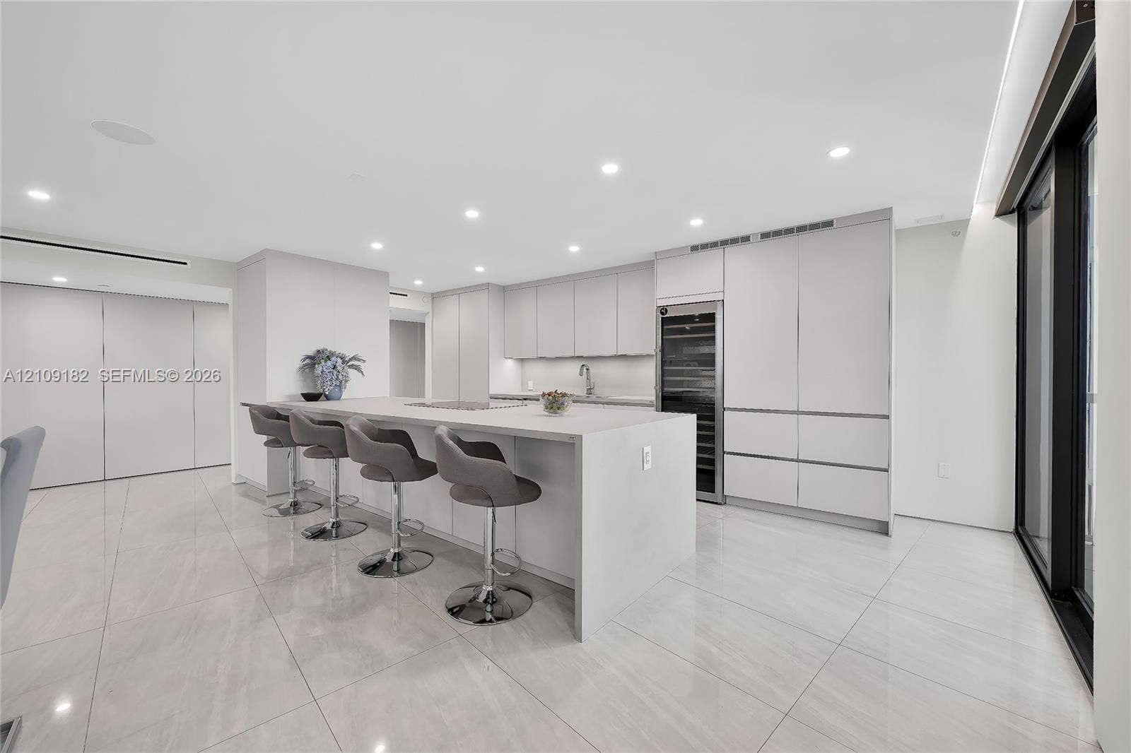 Kitchen featuring a waterfall island with stone countertop, flat-panel cabinetry, integrated wine refrigeration, recessed ceiling lighting, and polished stone flooring