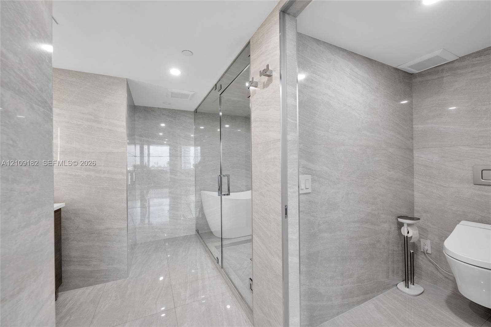 Bathroom featuring floor-to-ceiling large-format stone-finish tile, a glass-enclosed shower area, a freestanding soaking tub, and a wall-mounted toilet