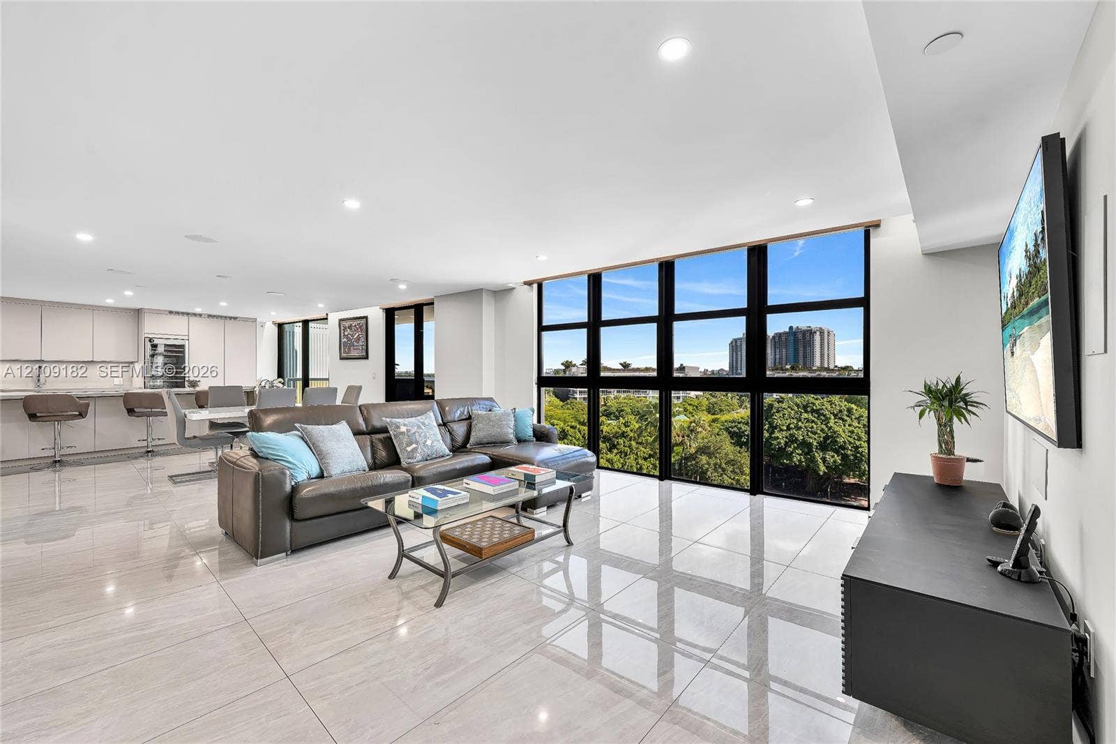Floor-to-ceiling black-framed windows, large-format tile flooring, recessed ceiling lighting, and built-in kitchen cabinetry with stone countertops