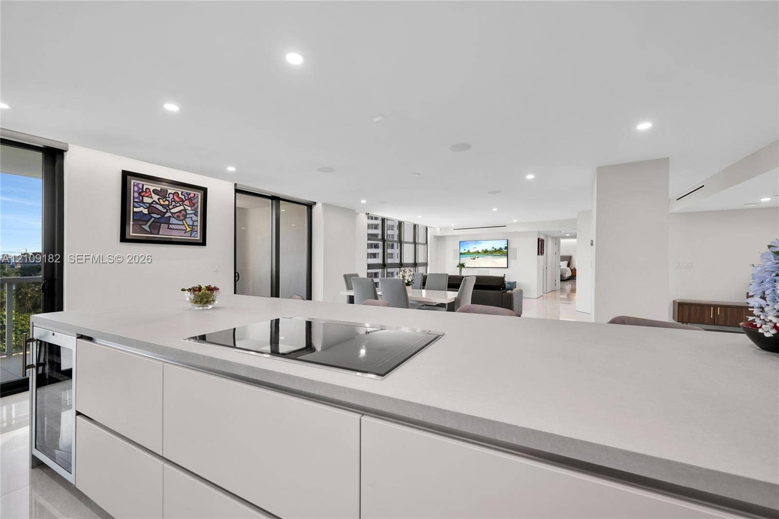Kitchen island featuring a flat-panel cabinetry base, integrated under-counter beverage refrigerator, and an inset electric cooktop with a smooth stone-finish countertop