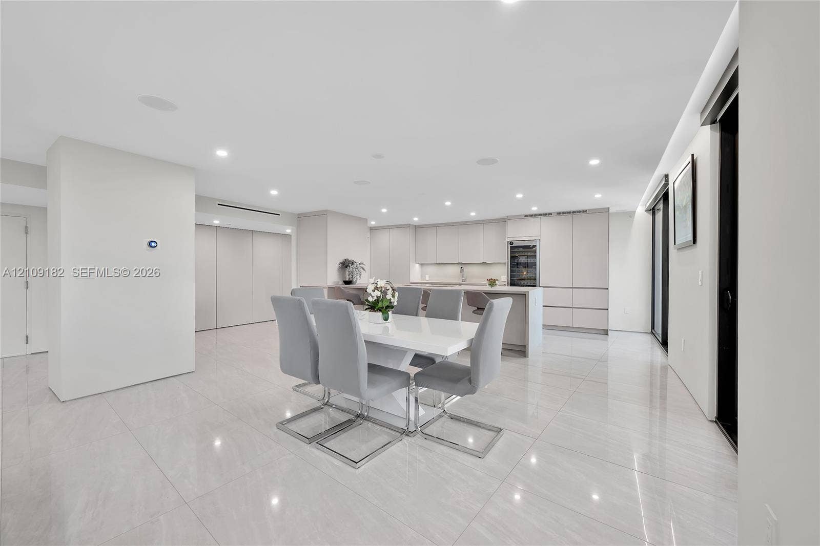 Open-concept kitchen and dining area featuring large-format tile flooring, flat-panel cabinetry, a central island with integrated seating, recessed lighting, and a built-in wine refrigerator