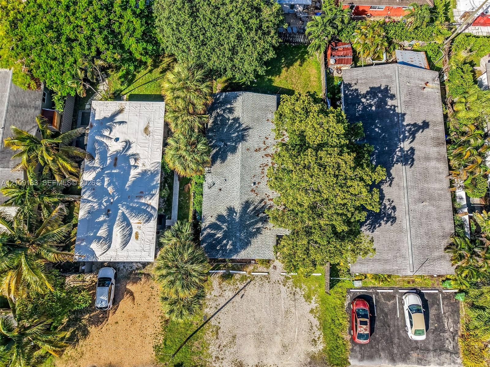 1009 NE 17th Court, Fort Lauderdale, FL 33305 Aerial view of three structures featuring pitched shingle roofing, mature palm trees, and an asphalt parking area