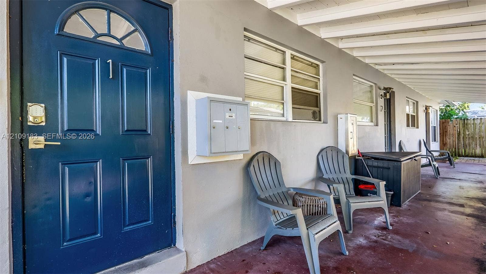 1009 NE 17th Court, Fort Lauderdale, FL 33305 Covered exterior walkway featuring a solid-panel door with an arched window inlay, horizontal sliding windows, and a wall-mounted metal mailbox