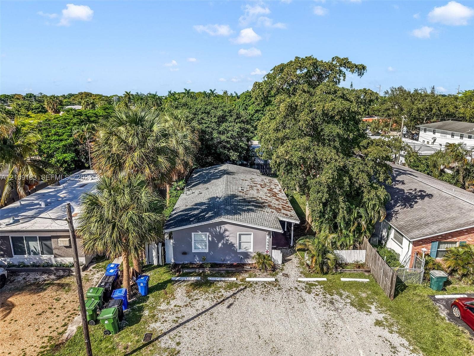 1009 NE 17th Court, Fort Lauderdale, FL 33305 Single-story residence featuring a gray exterior finish, gabled roofline, and gravel driveway